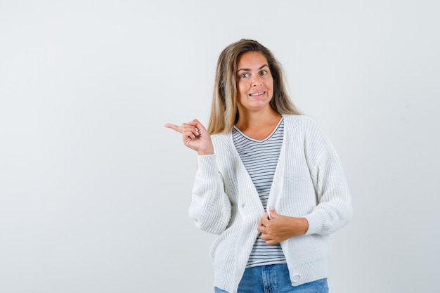 Belle femme pointant vers le côté en veste et à la vue confuse, de face.