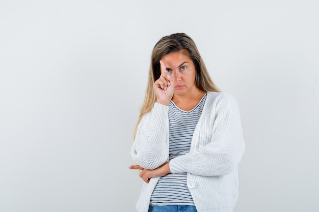 Belle femme pointant vers le haut en veste et à la recherche de confiance. vue de face.