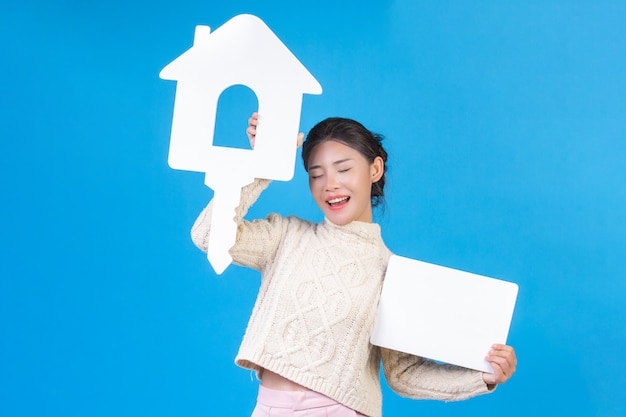 Une belle femme portant une nouvelle chemise, un tapis blanc à manches longues portant le symbole de la maison et un panneau blanc sur un bleu. Commerce .