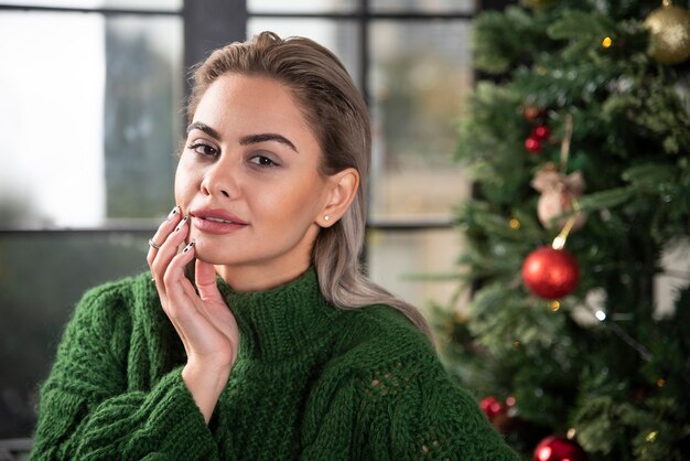 Belle femme portant un pull chaud posant près de l'arbre de Noël.