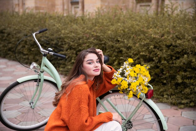 Belle femme posant à côté de vélo avec des fleurs à l'extérieur