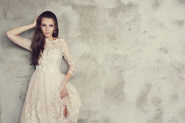 Belle femme posant avec une élégante robe blanche, fond de mur