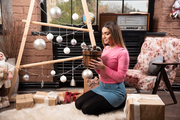 Belle femme posant avec un seau de pommes de pin à la maison.