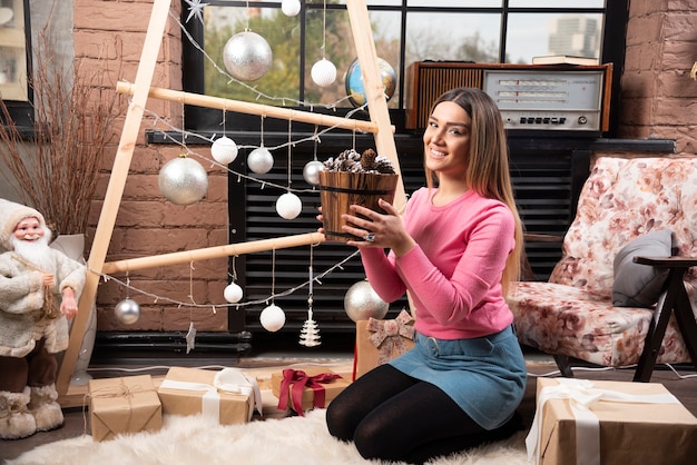 Belle femme posant avec un seau de pommes de pin à la maison.