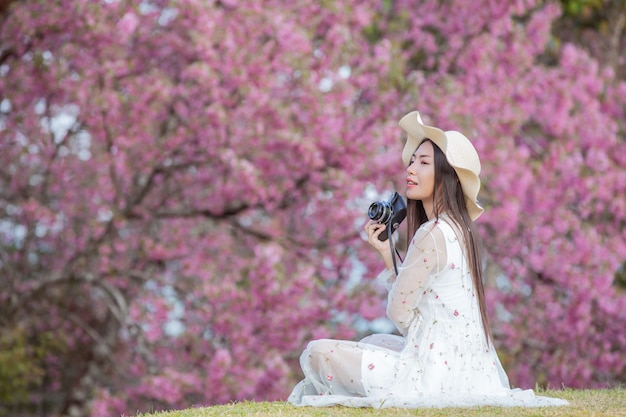 Une belle femme prend une photo avec un appareil photo argentique dans le jardin de fleurs de Sakura.