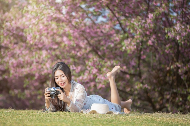 Une belle femme prend une photo avec un appareil photo argentique dans le jardin de fleurs de Sakura.