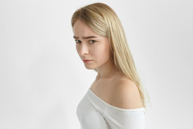 Belle femme de profil avec des cheveux lâches blonds posant isolé ayant une expression faciale tendue inquiète, éprouvant des problèmes, souffrant de maux de tête, regardant et fronçant les sourcils