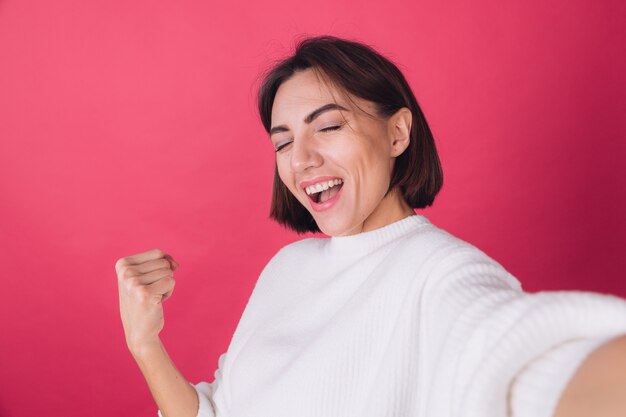 Belle femme en pull blanc décontracté sur mur rouge