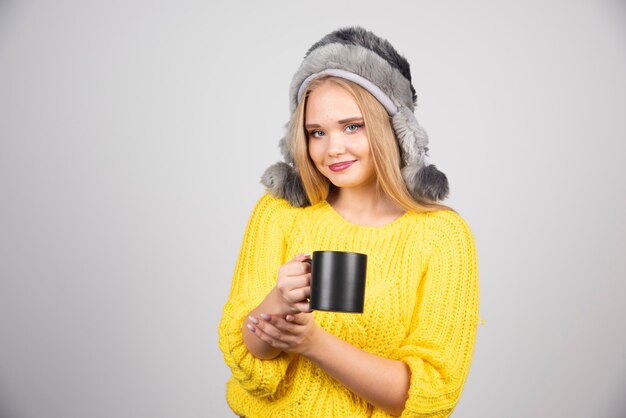 Belle femme en pull jaune tenant une tasse de thé.