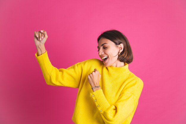 Belle femme en pull jaune vif isolé sur rose heureux sourire en mouvement danse excitée