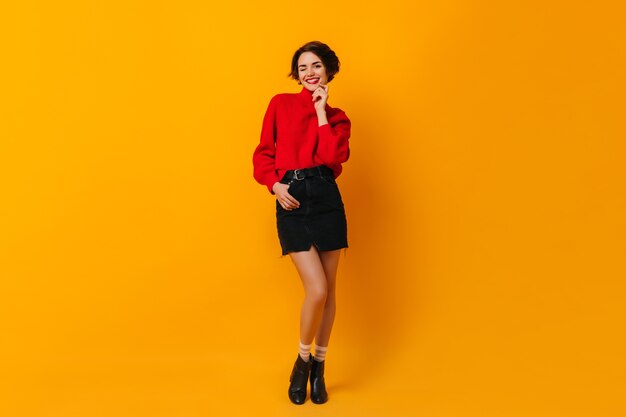 Belle femme en pull rouge debout sur un mur jaune