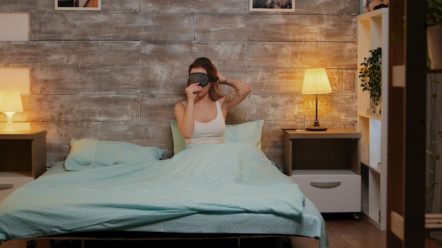 Belle femme en pyjama utilisant son téléphone avant d'aller dormir. Masque de sommeil.