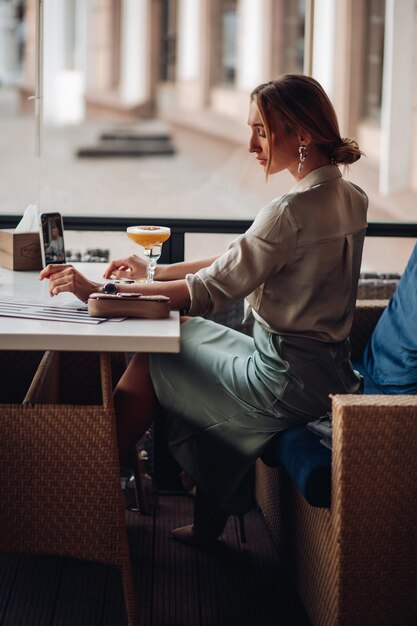 Belle femme de race blanche aux cheveux blonds prend une photo d'elle-même avec un cocktail dans un café