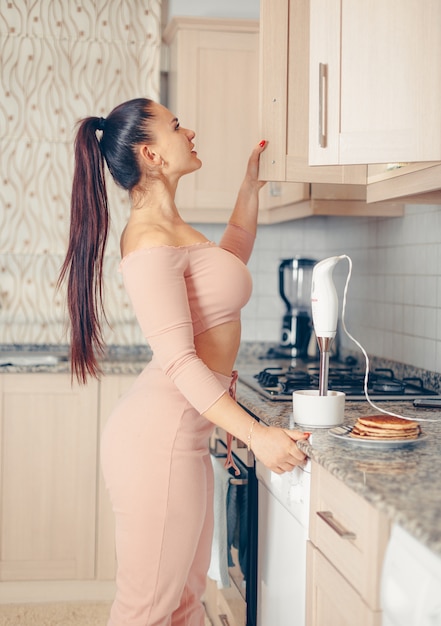 Belle femme à la recherche de quelque chose dans la cuisine en crop top rose saumon et pantalon