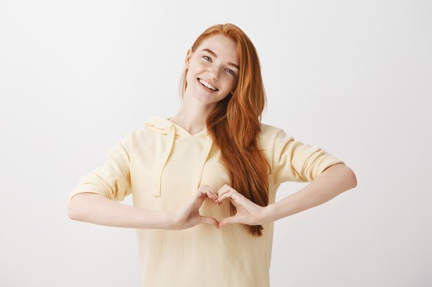 Belle femme redead montrant le geste du coeur et souriant