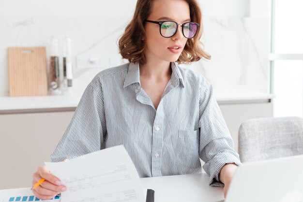 belle femme réfléchie dans des verres et chemise rayée travaillant avec des documents à la maison