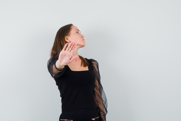 Photo gratuite belle femme regardant ailleurs tout en montrant le geste d'arrêt en chemisier noir et à la hauteur. vue de face. espace pour le texte