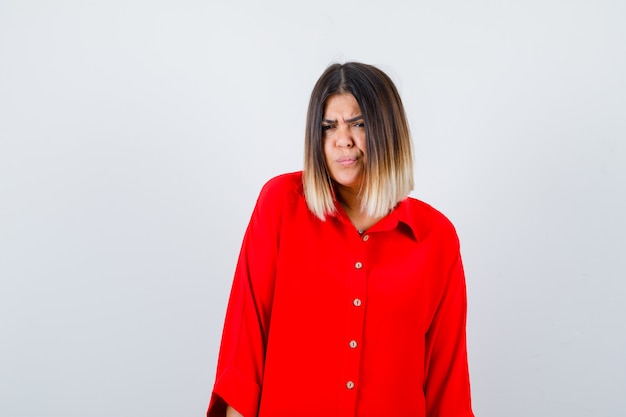 Belle femme regardant la caméra en fronçant les sourcils en chemisier rouge et l'air pensif. vue de face.