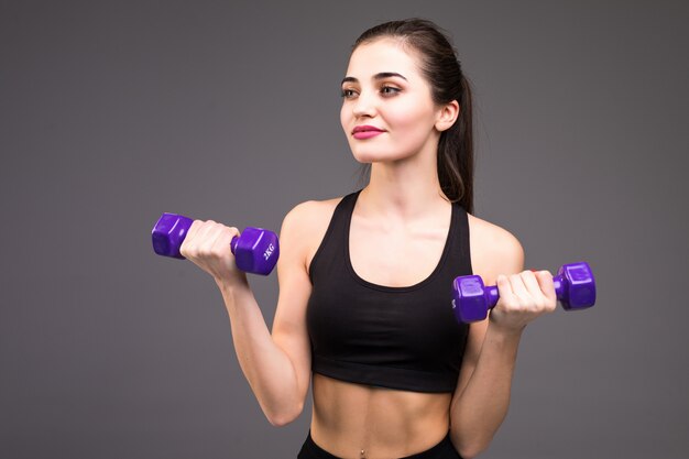 Belle femme de remise en forme faire des exercices de tonification avec des haltères sur un mur gris