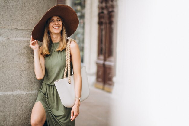 Photo gratuite belle femme en robe et chapeau debout par architecture