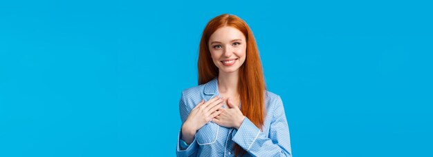 Belle femme rousse féminine avec de longs cheveux roux portant un pyjama tenir la main sur le cœur et souriant