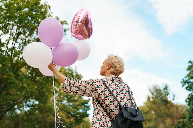 Belle femme avec sac à dos marchant heureux avec des ballons roses dans le parc. Concept de liberté et de femmes en bonne santé.