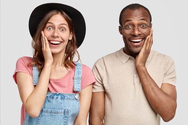 Photo gratuite belle femme satisfaite et heureuse et son homme touchent les joues, expriment des émotions positives, se tiennent côte à côte, isolés sur un mur blanc