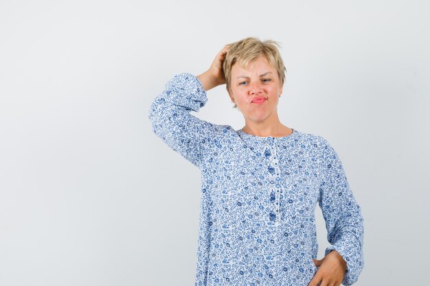 Belle femme se gratter la tête en chemisier à motifs et à la recherche compliquée. vue de face.