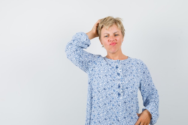 Belle femme se gratter la tête en chemisier à motifs et à la recherche compliquée. vue de face.