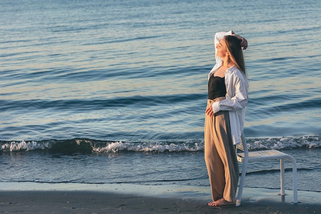 Une belle femme se tient près de la mer au coucher du soleil