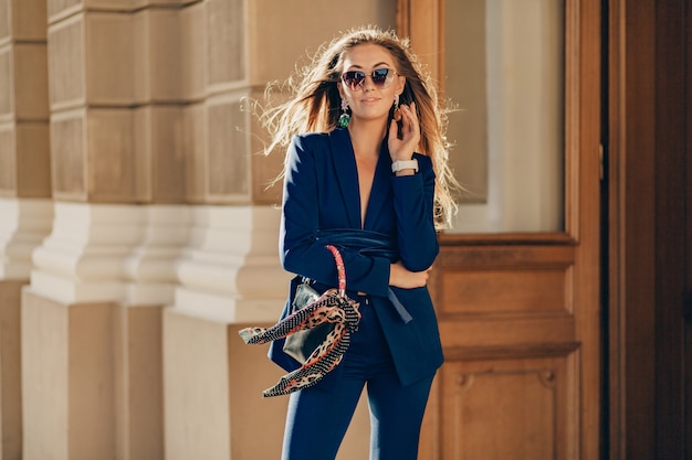 Belle femme souriante habillée en costume élégant et lunettes de soleil rue marche souriant par temps ensoleillé