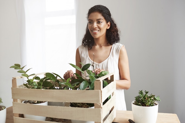 Photo gratuite belle femme souriante en prenant soin des plantes en boîte au lieu de travail mur blanc.