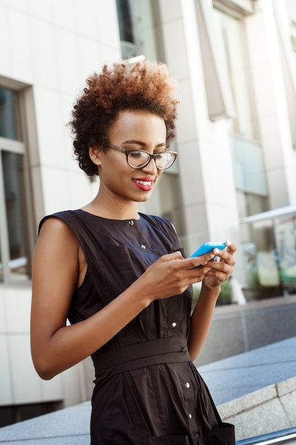 Photo gratuite belle femme souriante regardant téléphone marchant dans la ville