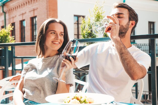 Belle femme souriante et son beau petit ami Bonne famille joyeuse Couple acclamant avec des verres de vin rouge à leur rendez-vous au restaurant Ils boivent de l'alcool au café véranda dans la rue