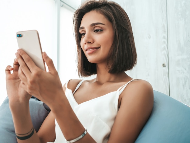 Photo gratuite belle femme souriante vêtue d'un pyjama blanc. femme insouciante assise sur une chaise de sac souple.