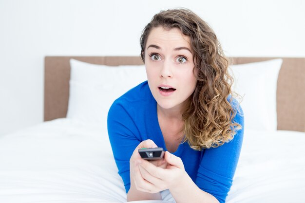 Belle femme surpris regardant la télévision sur le lit