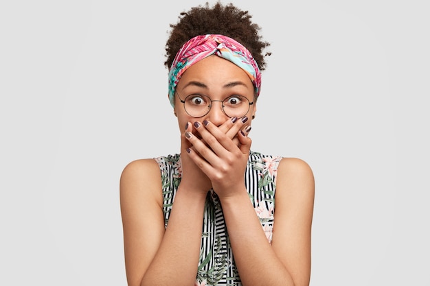 Belle femme surprise couvre la bouche avec les deux paumes, essaie d'arrêter le son fort produit par la peur, regarde les yeux avec des écouteurs