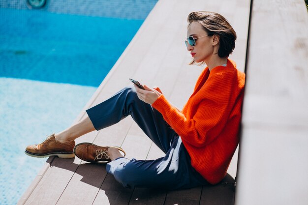 Belle femme avec téléphone assis au bord de la piscine