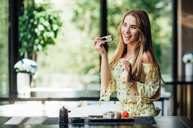 Belle femme tenant des baguettes avec des sushis et posant