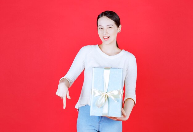 Belle femme tenant une boîte-cadeau et un doigt pointé vers le bas