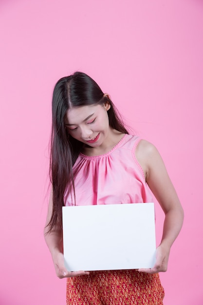 Belle femme tenant une feuille de tableau blanc sur un fond rose.