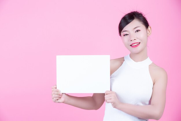 Belle femme tenant une feuille de tableau blanc sur un fond rose.