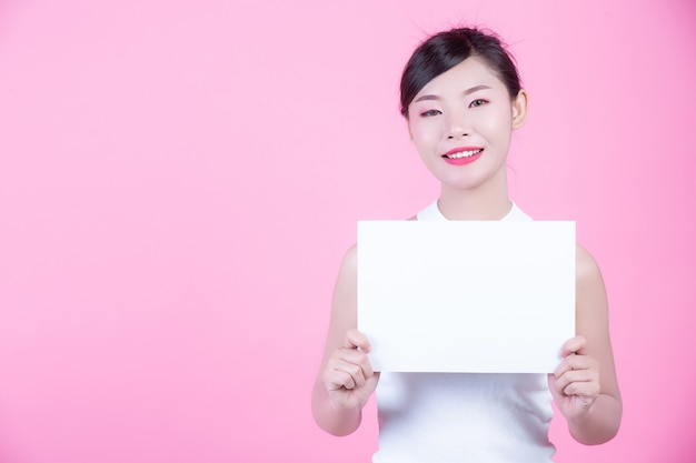 Belle femme tenant une feuille de tableau blanc sur un fond rose.