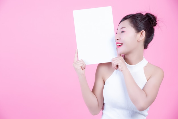 Belle femme tenant une feuille de tableau blanc sur un fond rose.