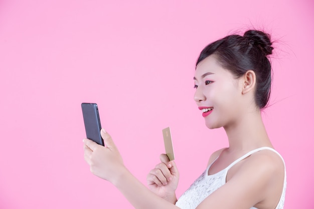 Belle femme tenant un smartphone et une carte sur un fond rose