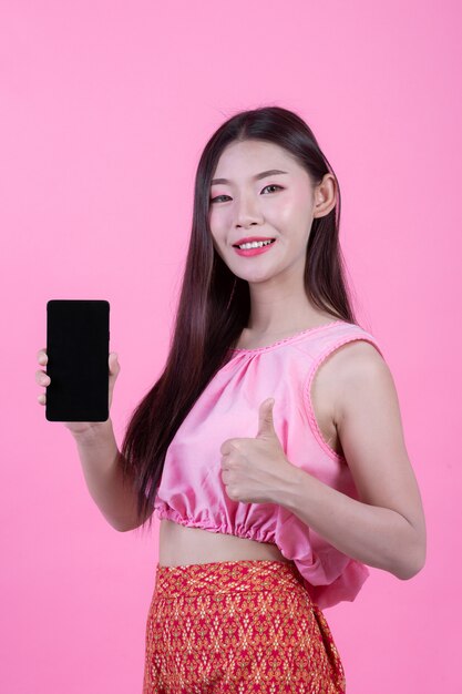 Belle femme tenant un smartphone sur un fond rose.