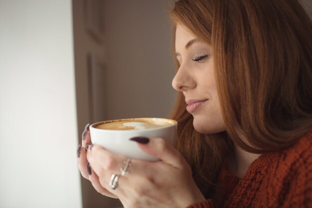 Belle femme tenant une tasse de café à la fenêtre