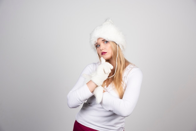 Belle femme en tenue d'hiver posant sur un mur gris.