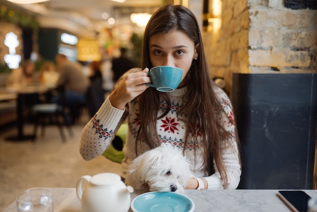 Belle femme tient son chien mignon, buvant du café et souriant au café