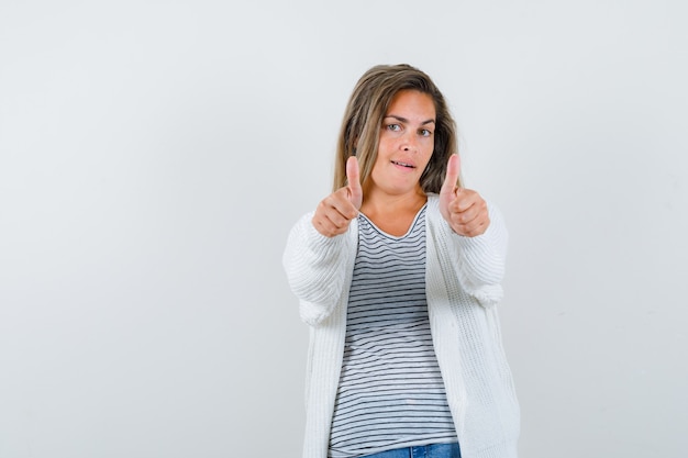 Belle femme en veste montrant les pouces vers le haut et l'air satisfait, vue de face.